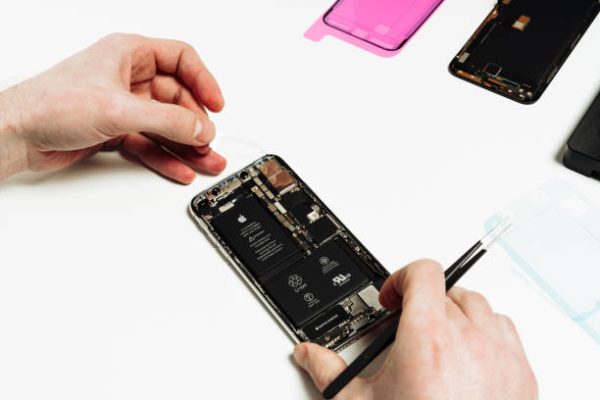 KYIV, UKRAINE - FEBRUARY 27 2019: Smart Phone Battery Change Repair Maintenance. Repairman Hand Fix Smartphone Back Part Disassemble with Tweezers. Mobile Cellphone Assembly. Technician Work